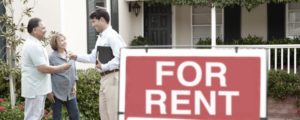 real estate agent handing house keys to couple by a for rent sign